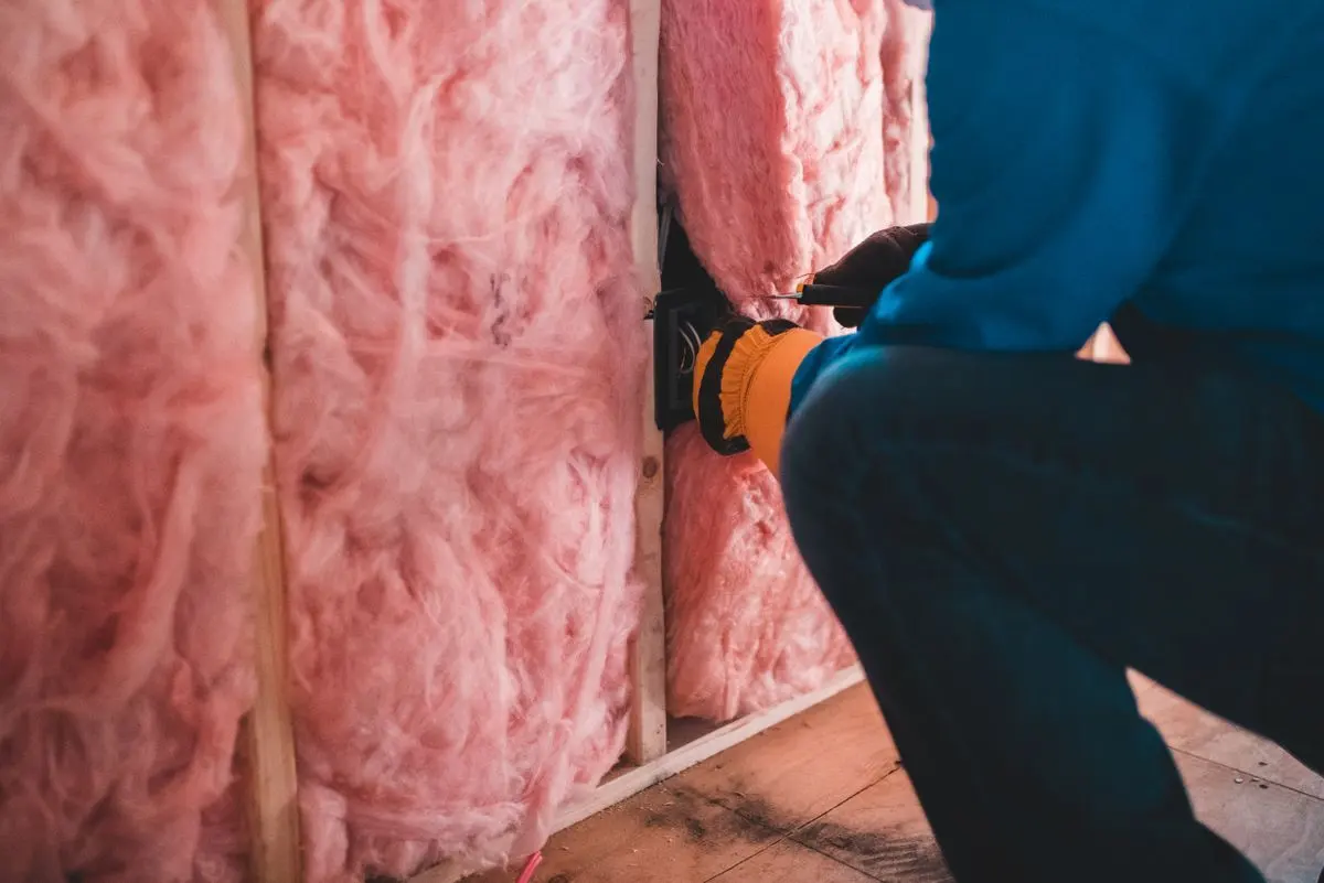 Installer fitting pink fiberglass batt insulation between wall studs
