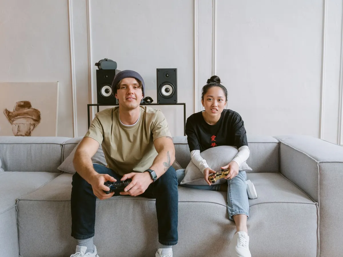 Couple playing video games together on a gray couch in a bright living room