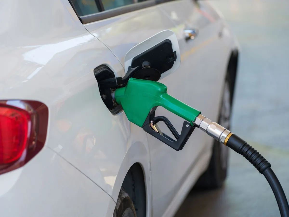 Green fuel nozzle refueling a white car at a gas station