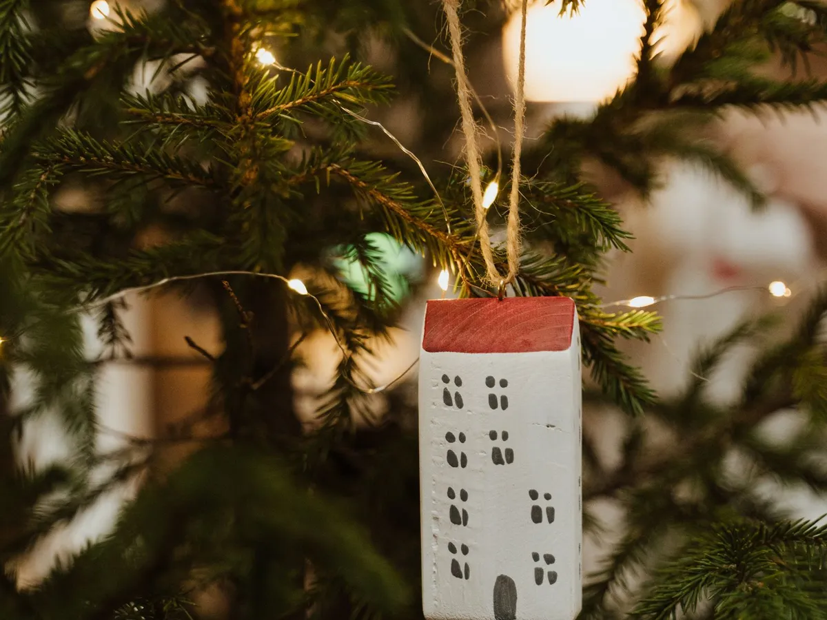 House-shaped ornament hanging on a Christmas tree with twinkling lights