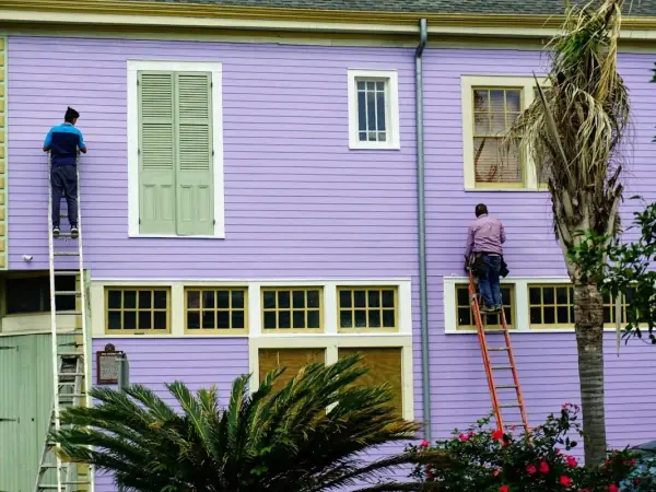 Two workers on ladders painting and repairing the siding of a two-story house